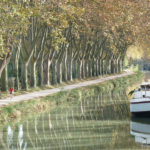 Canal du Midi: bucolic scenery of a canal lined with trees and a barge parked on the side