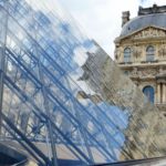 louvre pyramid with reflections of the stone building against the glass