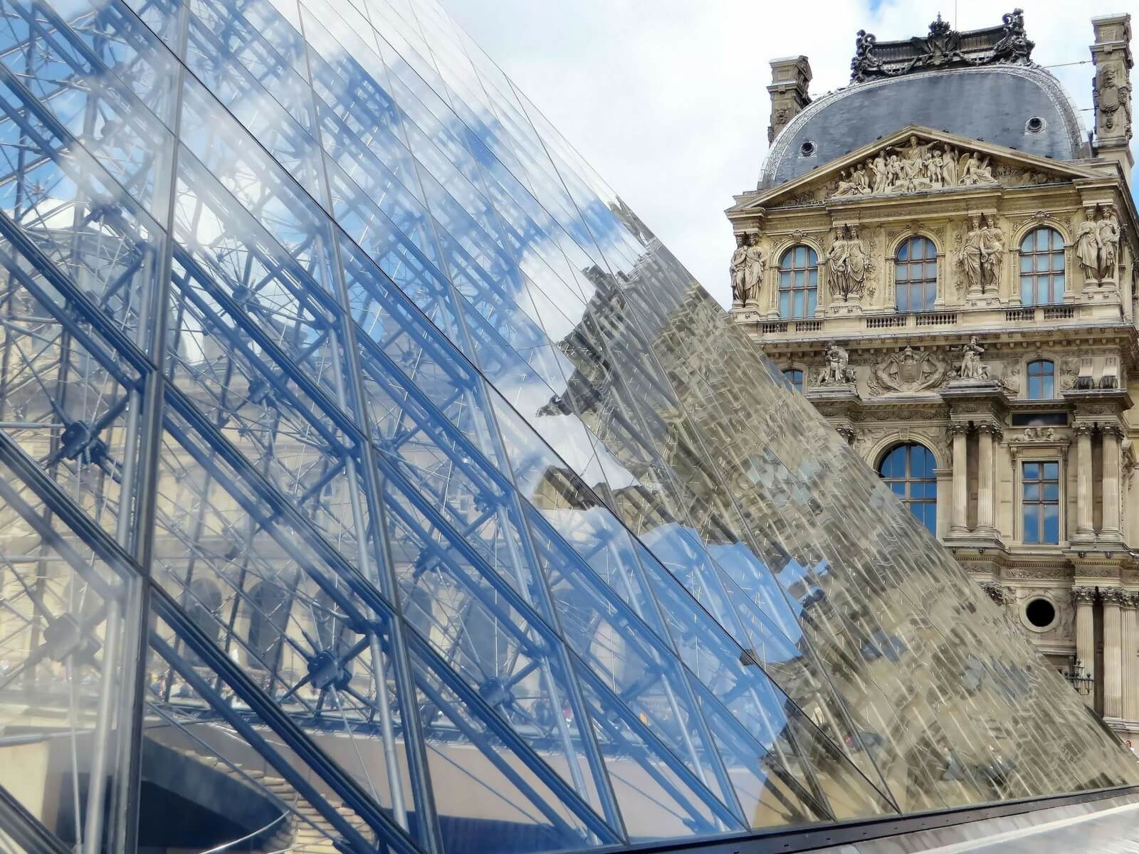 louvre pyramid with reflections of the stone building against the glass