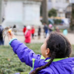 little girl wearing a purple coat feeding a bird in front of Notre Dame in Paris