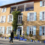 Man and woman visiting the town of Carla-Bayle and walking by a beautiful home with blue shutters and blue planters