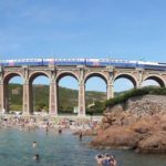 train in france going over a bridge and bathers in a river at the bottom of the bridge