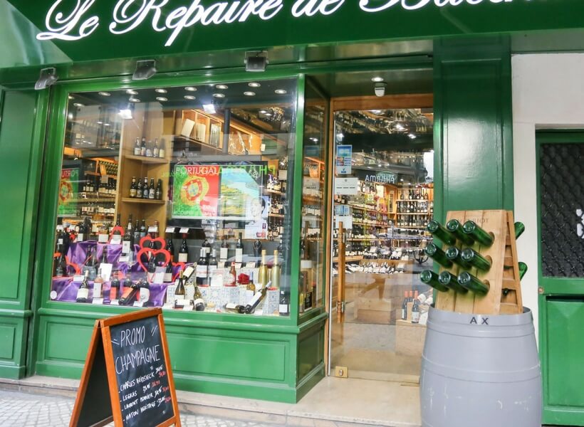 wine store in paris, window display with many wine bottles , promotional sandwich board and wine barrel outside