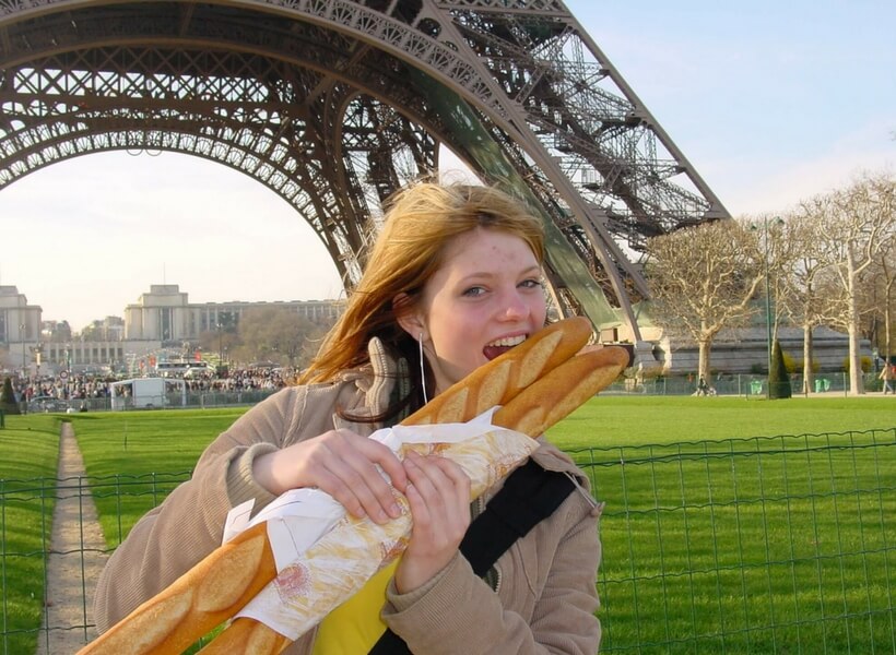 Young woman biting into a French baguette in front of the Eiffel Tower