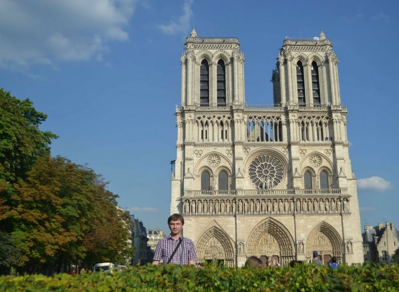 Visiting Paris in August: man posing in front of Notre Dame Cathedral on a summer day