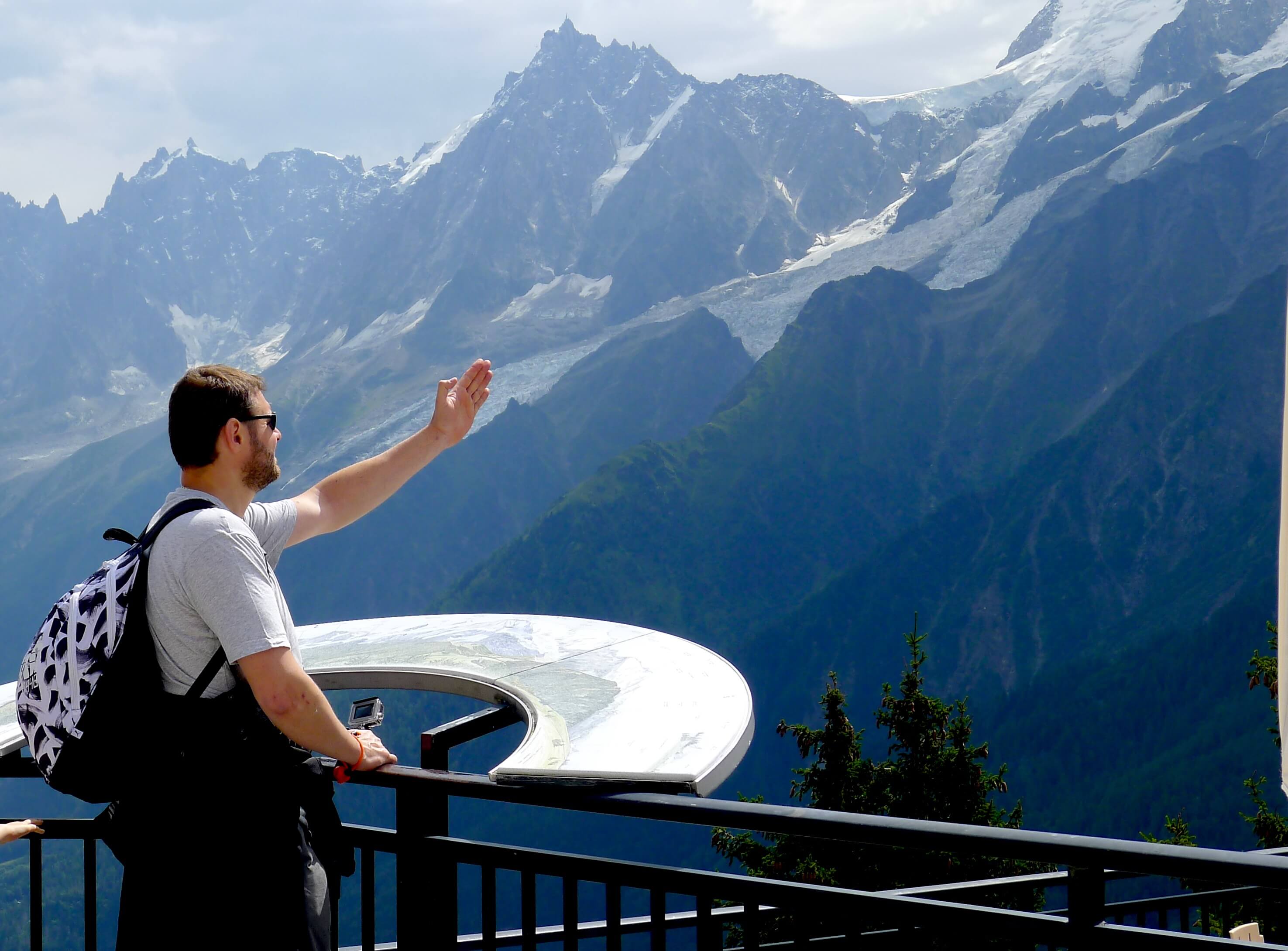 man with backpack looking at a table of orientation in the french mountains