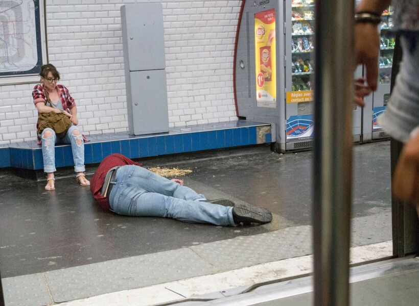 man lying on the metro floor, he has vomited and a woman is making sure he is not chocking