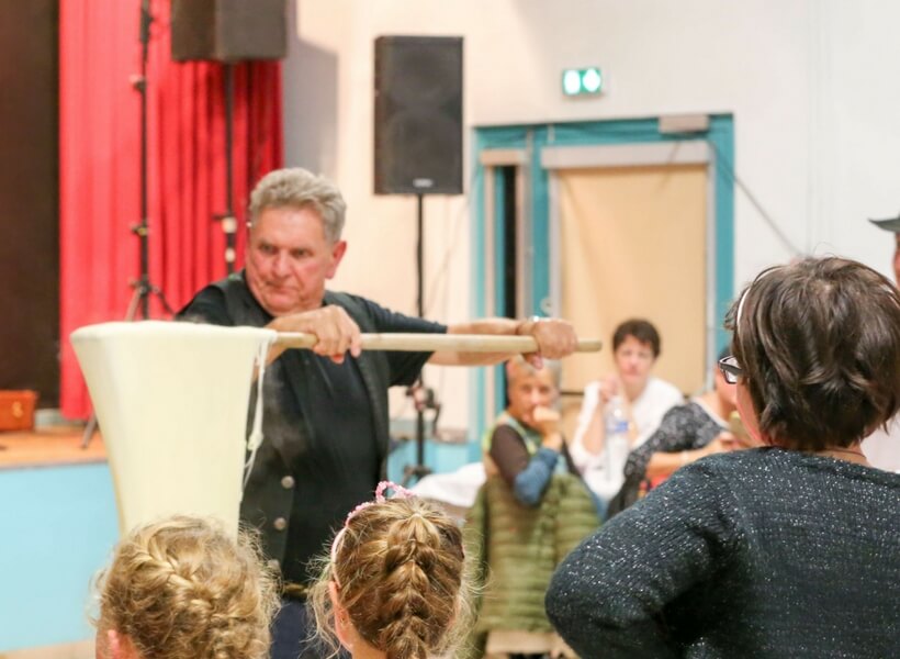 man demonstrating the stringy nature of aligot with two young girls and a woman observing him