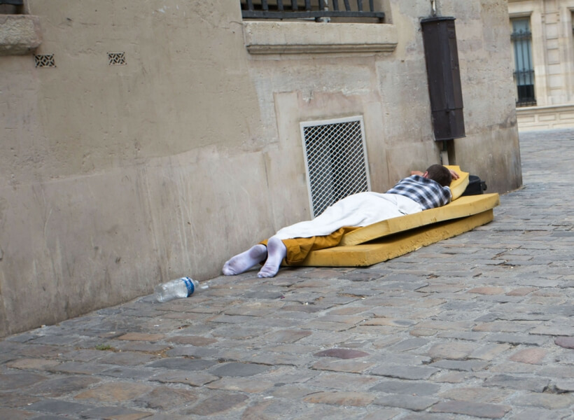 man sleeping on a paris street, he is lying on two foam pads and his face is turned towards the wall