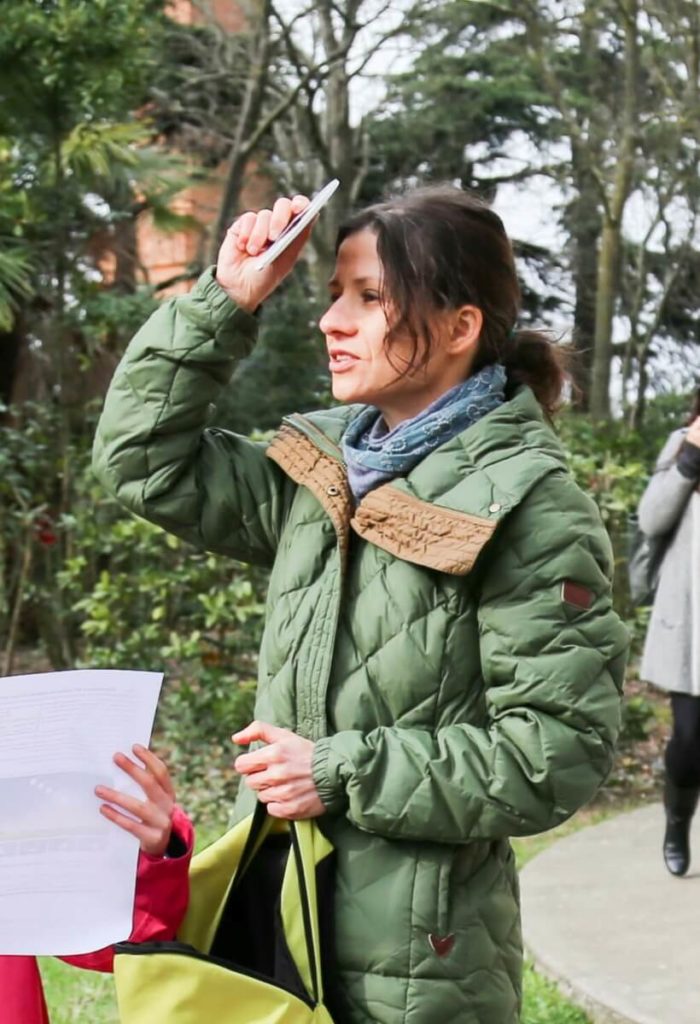 French woman in her 20s wearing a green coat and a blue scarf