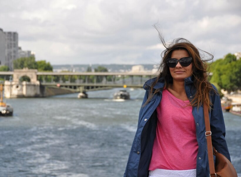 woman wearing a pink t-shirt and a blue wind breaker posing for a photo on a bridge in Paris