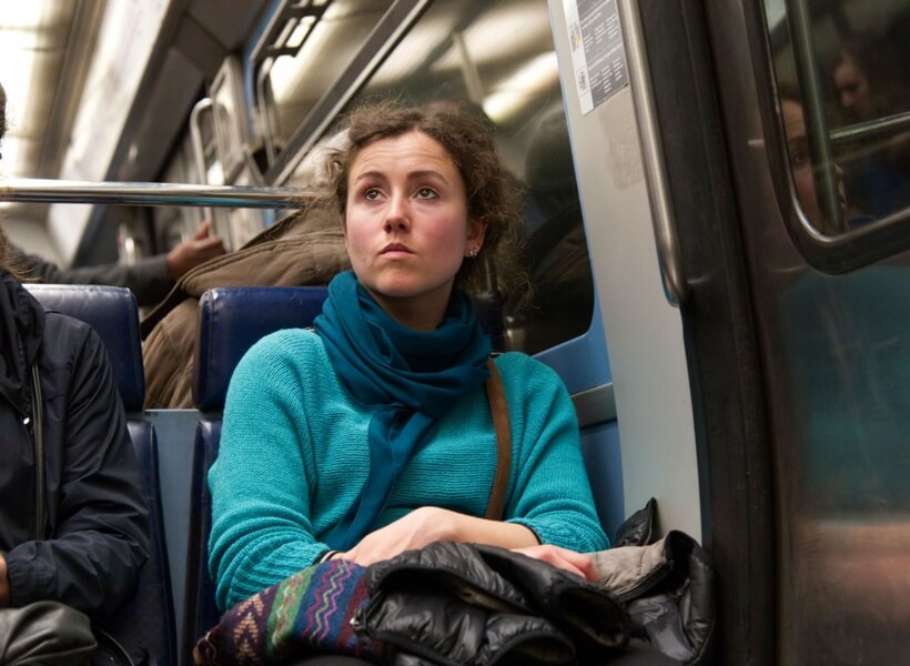 woman in her late 20s wearing a light blue shirt and a dark blue scarf on the metro in paris