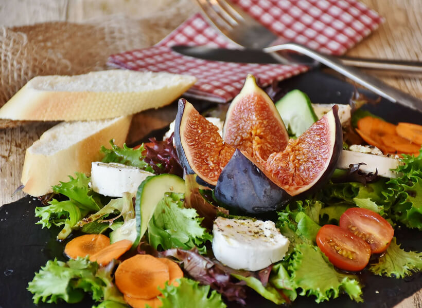 Salad with greens, carrots, avocado, cherry tomatoes, goat cheese and a fig