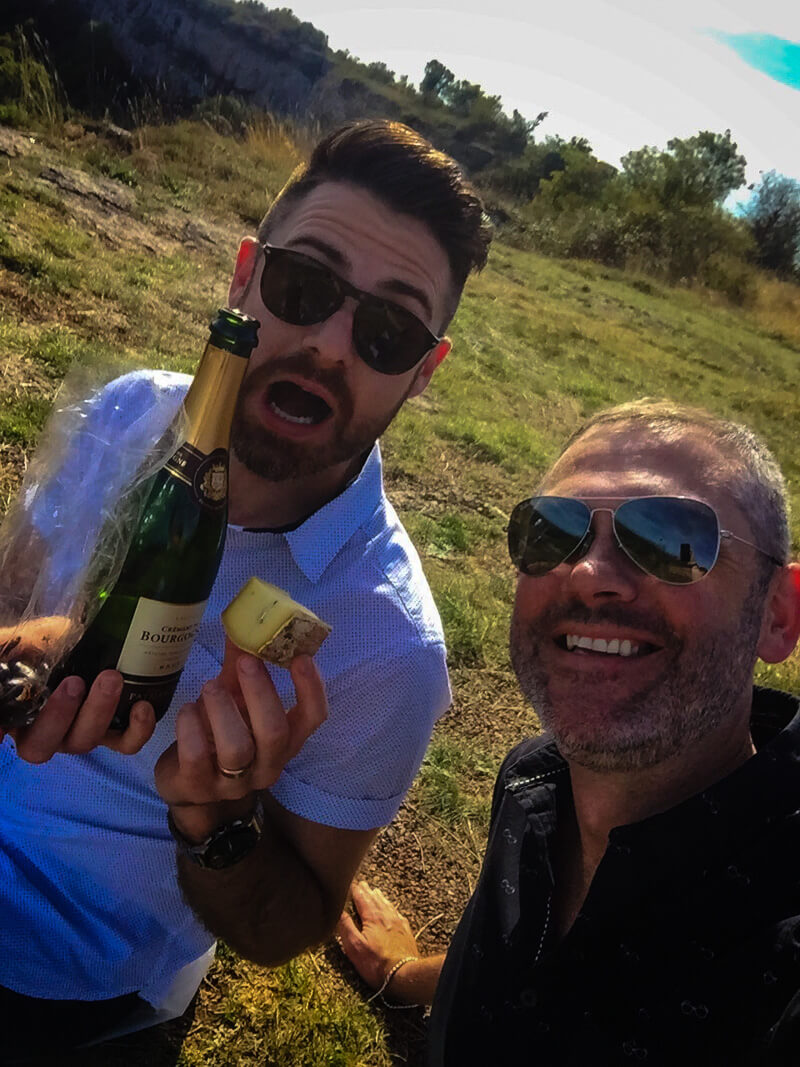 Two men with a bottle of wine and some cheese