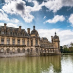 Chateau of Chantilly surrounded by water with a dramatic blue sky and white clouds