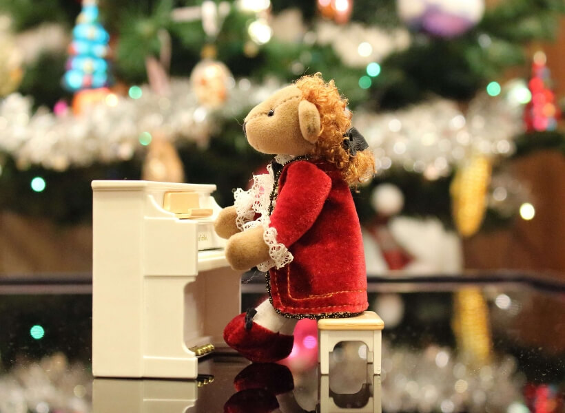 Tiny white piano with cloth puppet sitting on a bench in front of the piano: French Christmas Songs Transcript Episode