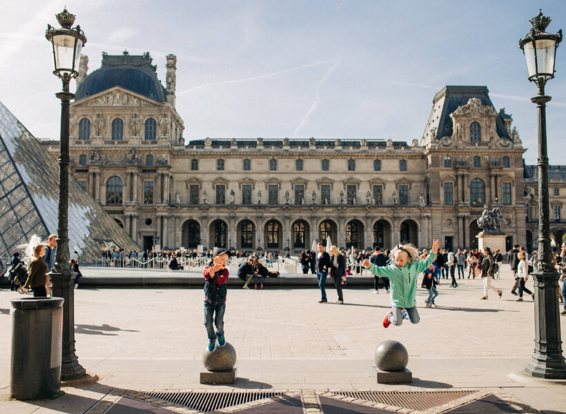 children jumping up and having a good time in front of the Louvre Museum: Great Destinations in France for Families episode