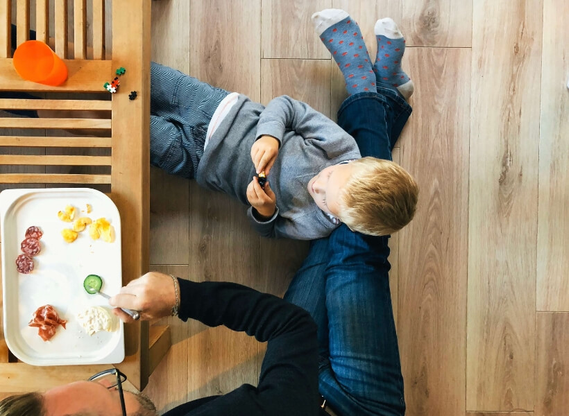 father sitting on the ground enjoying some lunch and boy resting on father's legs, shot from above: vacation photos episode