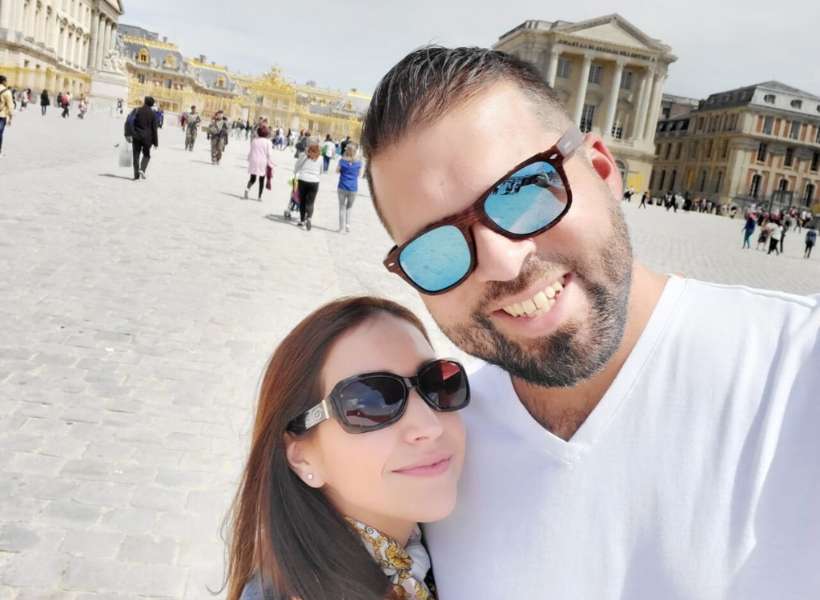 Emily and her husband doing a selfie in front of Versailles while on their honeymoon in Paris