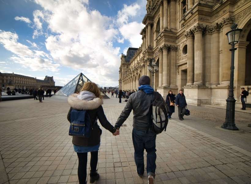 Man and woman holding hands walking towards the Louvre Museum: Best Practices When Preparing a Trip to France episode