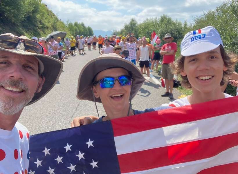 Melinda, Sean and their son holding an American flag. Watching a stage of the Tour de France in France episode