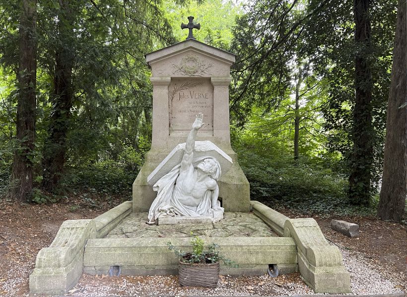 Jules Verne's grave in Amiens: a man reaches out of the grave with his right arm extended towards the sky and a book on his back.